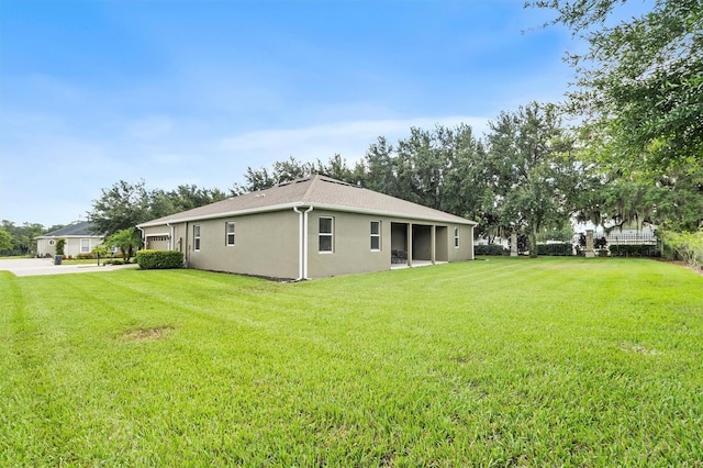 rear view of house with a yard, an attached garage, driveway, and stucco siding