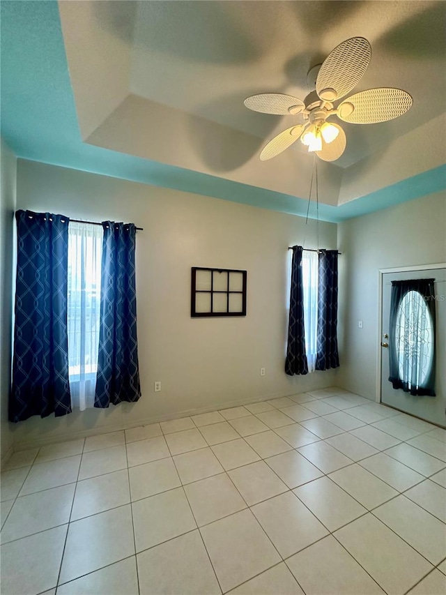 empty room featuring light tile patterned flooring, ceiling fan, and a raised ceiling