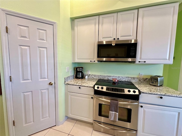 kitchen featuring light tile patterned flooring, appliances with stainless steel finishes, white cabinetry, and light stone counters