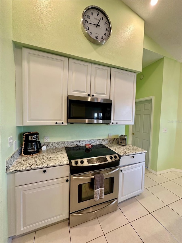 kitchen with light tile patterned floors, appliances with stainless steel finishes, white cabinetry, and baseboards