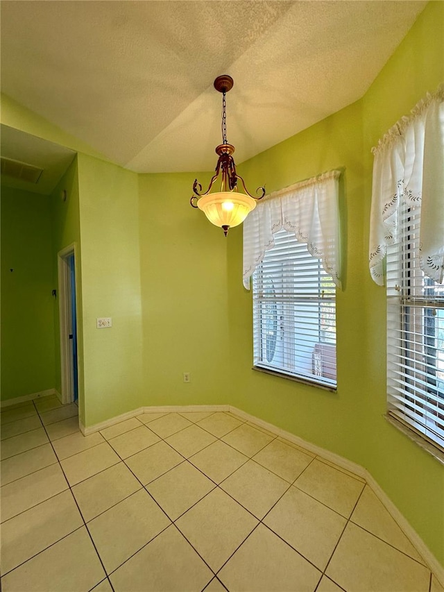 unfurnished dining area featuring light tile patterned flooring, a healthy amount of sunlight, baseboards, and a textured ceiling