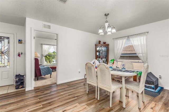 dining room featuring baseboards, visible vents, light wood finished floors, an inviting chandelier, and a textured ceiling