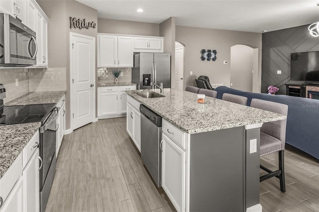 kitchen with a kitchen island with sink, light wood-type flooring, stainless steel appliances, and a breakfast bar