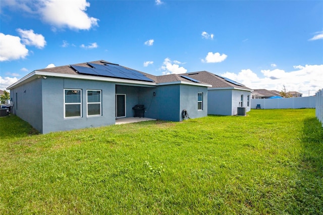 back of house featuring central air condition unit, a lawn, a patio, and solar panels