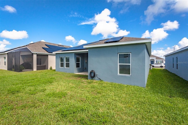 rear view of property featuring a lawn, solar panels, and a sunroom