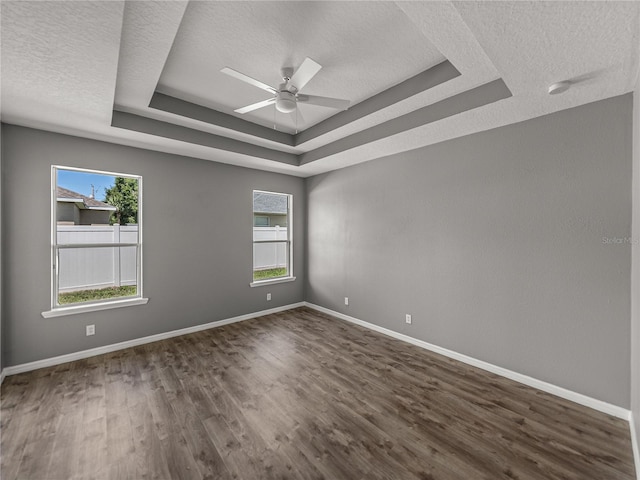 spare room with a textured ceiling, ceiling fan, dark hardwood / wood-style floors, and a tray ceiling