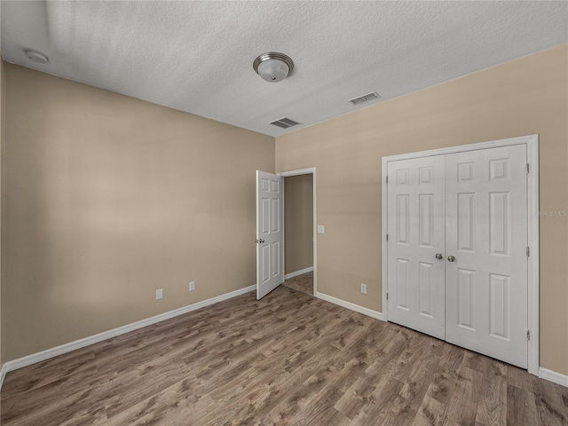 unfurnished bedroom featuring a textured ceiling, a closet, and wood-type flooring