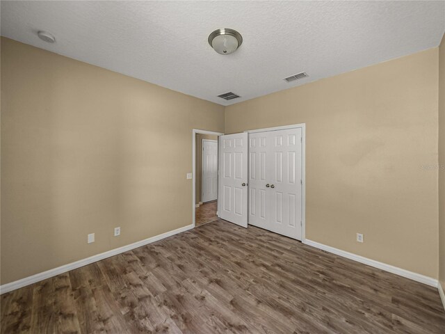 unfurnished bedroom featuring a textured ceiling, wood-type flooring, and a closet