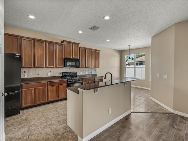 kitchen with a kitchen breakfast bar, decorative light fixtures, black appliances, an island with sink, and decorative backsplash