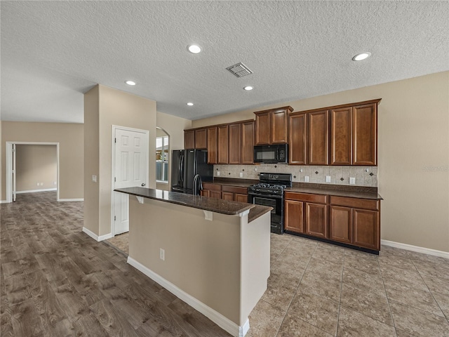 kitchen featuring sink, a kitchen breakfast bar, black appliances, a kitchen island with sink, and decorative backsplash