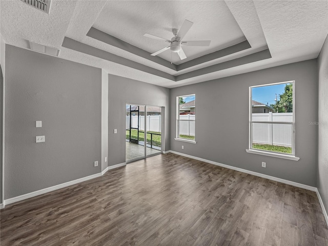 empty room with ceiling fan, a raised ceiling, a textured ceiling, and dark hardwood / wood-style floors