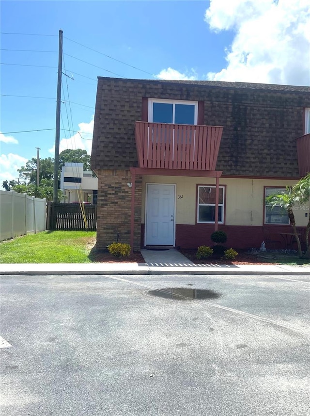 view of property with brick siding, mansard roof, a shingled roof, and fence