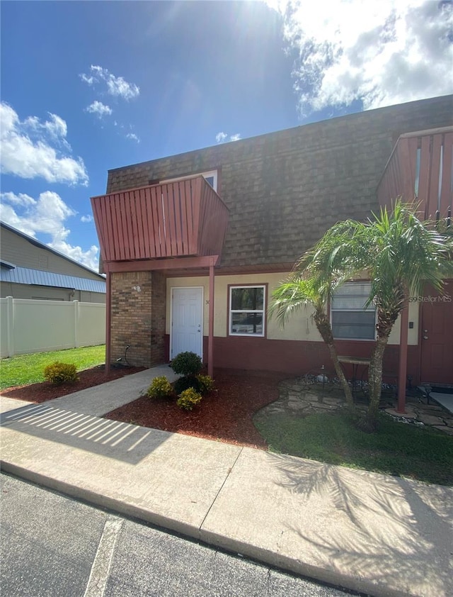 townhome / multi-family property featuring stucco siding, mansard roof, fence, a shingled roof, and brick siding