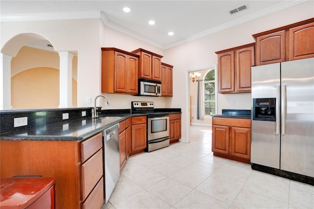 kitchen featuring dark stone counters, ornamental molding, sink, appliances with stainless steel finishes, and ornate columns