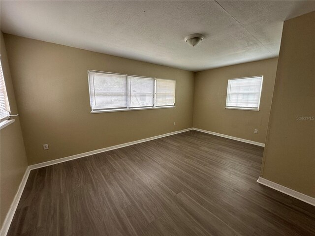 empty room featuring dark wood-type flooring, a textured ceiling, and plenty of natural light