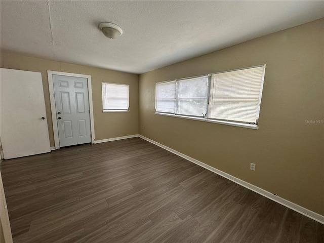 spare room featuring dark wood-style floors, a textured ceiling, and baseboards