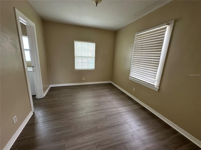 empty room featuring dark wood-type flooring, plenty of natural light, and baseboards