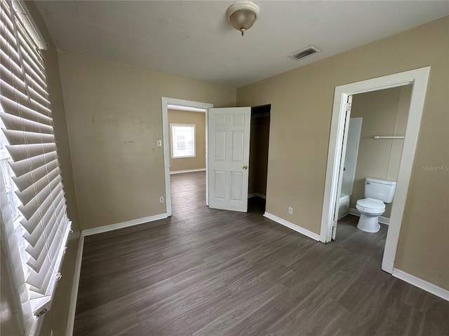 unfurnished bedroom featuring dark wood finished floors, visible vents, ensuite bathroom, and baseboards