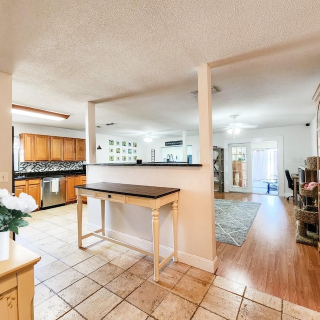 kitchen with light wood-type flooring, a kitchen breakfast bar, backsplash, stainless steel dishwasher, and a textured ceiling