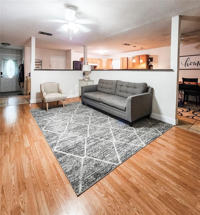 living room featuring wood-type flooring, a textured ceiling, and ceiling fan