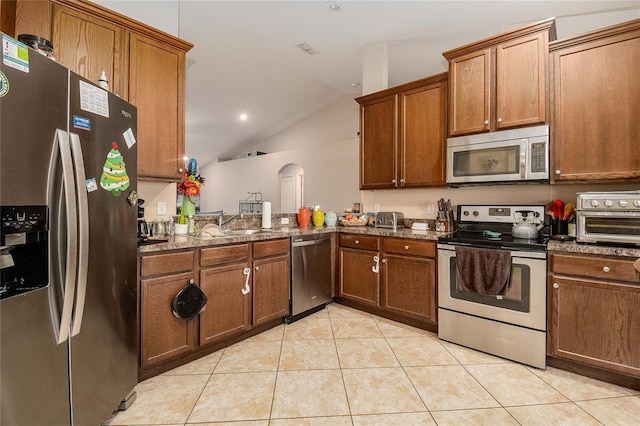 kitchen with light tile patterned floors, appliances with stainless steel finishes, kitchen peninsula, lofted ceiling, and dark stone counters