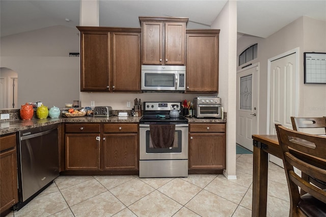 kitchen featuring vaulted ceiling, appliances with stainless steel finishes, dark stone counters, and light tile patterned flooring