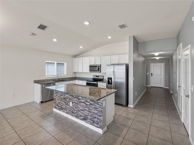 kitchen featuring white cabinets, appliances with stainless steel finishes, a center island, dark stone countertops, and sink