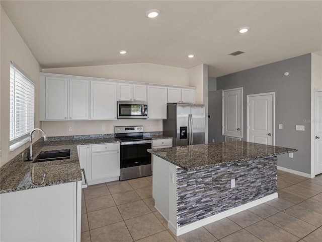 kitchen with white cabinetry, stainless steel appliances, sink, dark stone countertops, and a center island