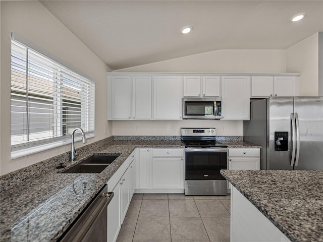 kitchen with vaulted ceiling, sink, white cabinetry, appliances with stainless steel finishes, and dark stone counters