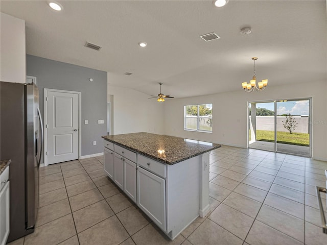 kitchen featuring dark stone countertops, a kitchen island, white cabinetry, stainless steel fridge, and ceiling fan with notable chandelier