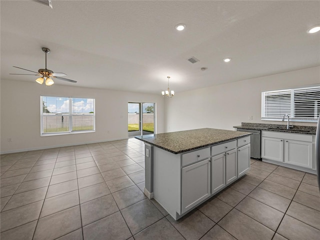 kitchen with stainless steel dishwasher, dark stone counters, ceiling fan with notable chandelier, white cabinets, and a center island