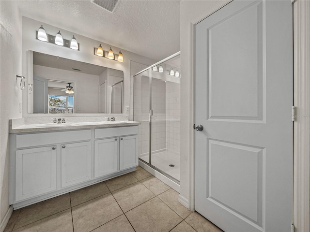 bathroom featuring ceiling fan, vanity, tile patterned flooring, a textured ceiling, and a shower with door