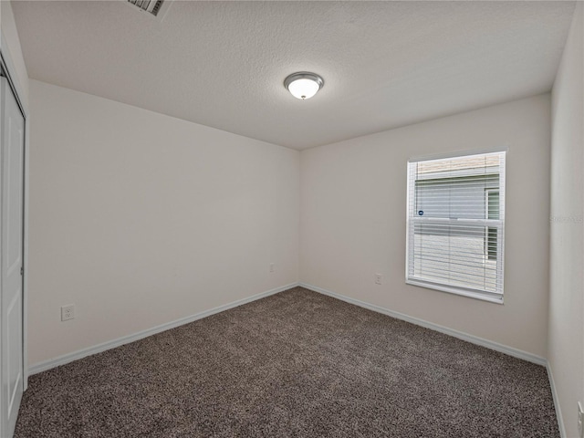 empty room with a textured ceiling and dark colored carpet