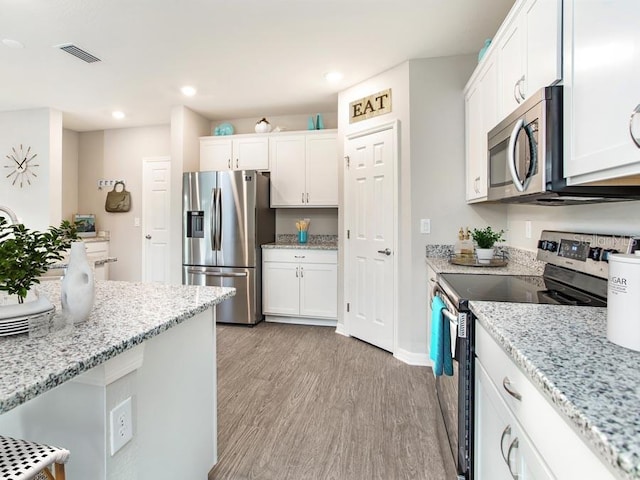 kitchen with light stone counters, appliances with stainless steel finishes, white cabinets, and light hardwood / wood-style floors