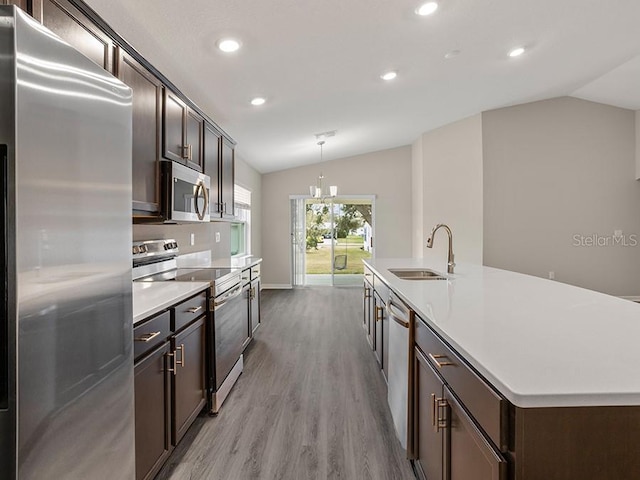 kitchen featuring a center island with sink, decorative light fixtures, lofted ceiling, and stainless steel appliances