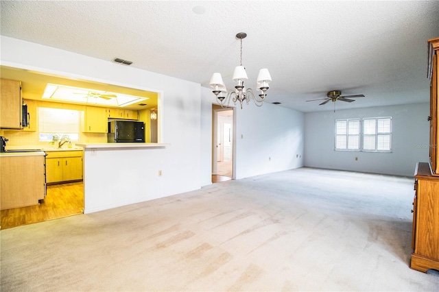 unfurnished living room featuring light colored carpet, ceiling fan with notable chandelier, and a textured ceiling