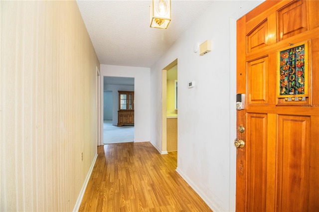 hall with a textured ceiling and light hardwood / wood-style flooring