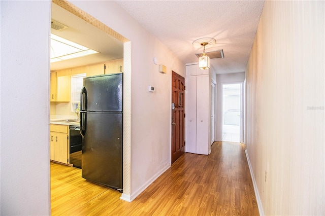 corridor featuring a textured ceiling, light wood-type flooring, visible vents, and baseboards