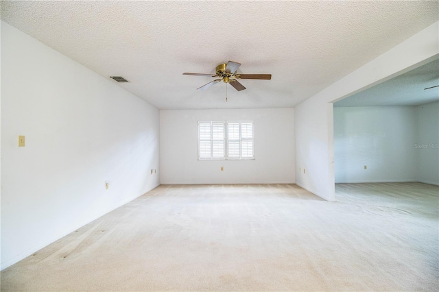 unfurnished room featuring light carpet, a textured ceiling, visible vents, and a ceiling fan