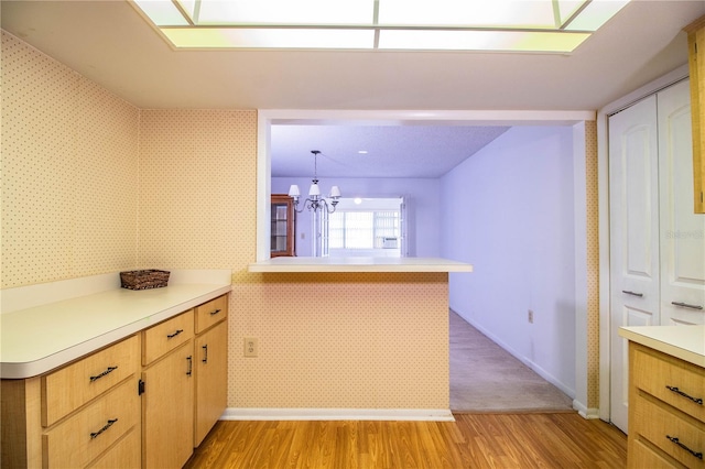 kitchen featuring a chandelier, light wood-type flooring, light countertops, and wallpapered walls