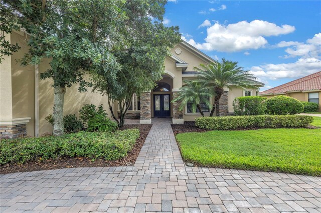 view of property hidden behind natural elements with french doors and a front yard