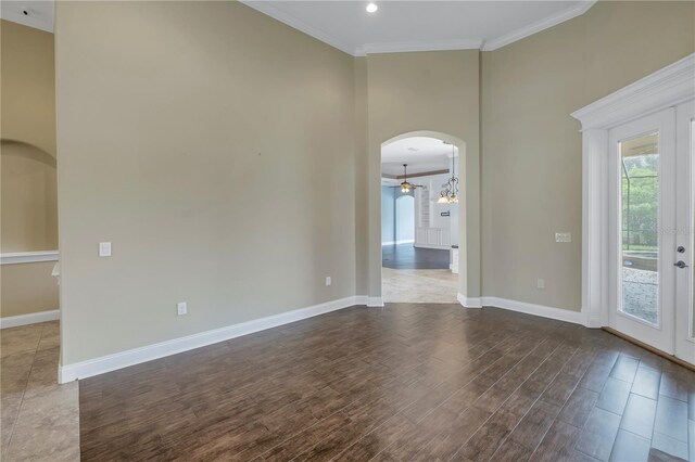 empty room with french doors, wood-type flooring, a high ceiling, a notable chandelier, and crown molding