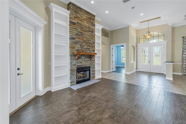 unfurnished living room with a fireplace, crown molding, french doors, built in shelves, and dark hardwood / wood-style floors