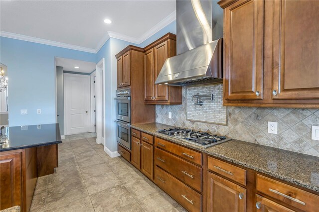 kitchen with tasteful backsplash, wall chimney exhaust hood, stainless steel appliances, dark stone countertops, and crown molding