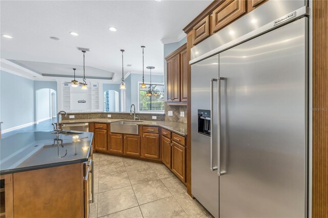 kitchen featuring pendant lighting, stainless steel built in fridge, dark stone counters, and sink