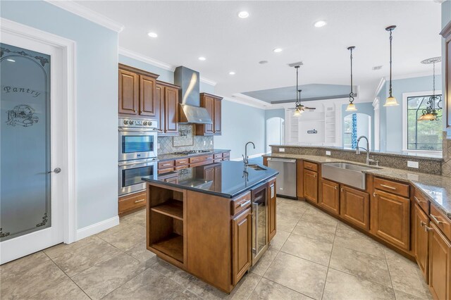 kitchen featuring sink, a kitchen island with sink, wall chimney exhaust hood, appliances with stainless steel finishes, and dark stone counters