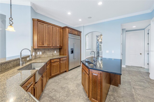 kitchen with backsplash, pendant lighting, a center island with sink, sink, and stainless steel built in fridge