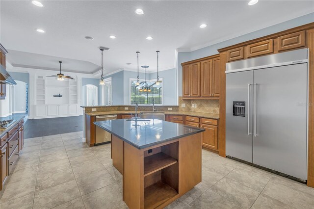 kitchen with pendant lighting, a center island with sink, appliances with stainless steel finishes, ornamental molding, and ceiling fan