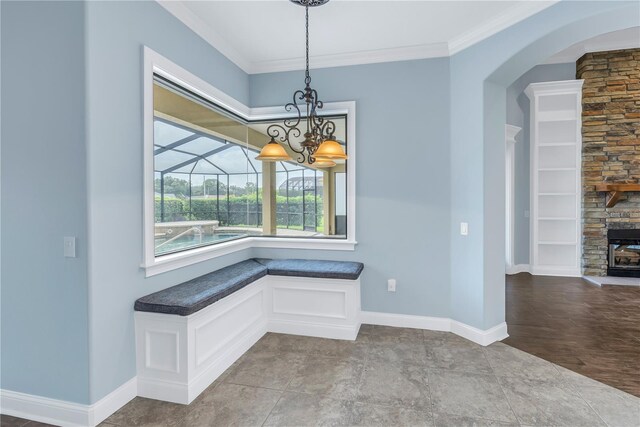 unfurnished dining area with a stone fireplace, an inviting chandelier, and ornamental molding