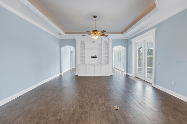 unfurnished living room featuring ceiling fan, a raised ceiling, built in features, dark hardwood / wood-style floors, and crown molding